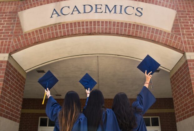 Tres mujeres con toga y birrete frente a la universidad