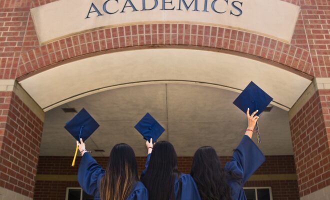 Tres mujeres con toga y birrete frente a la universidad